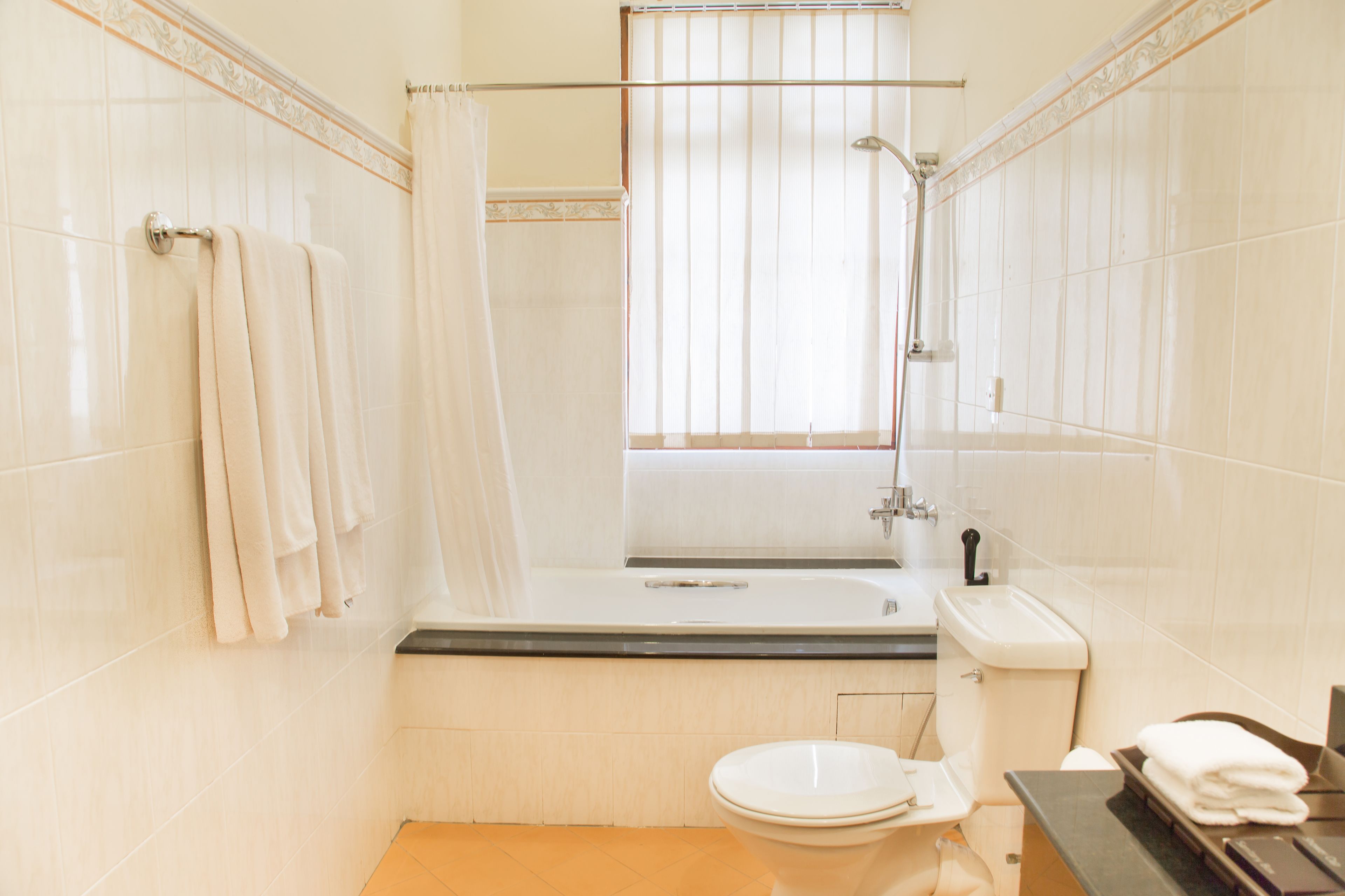 A bathroom with a bathtub, toilet, and a window with a shower curtain.
