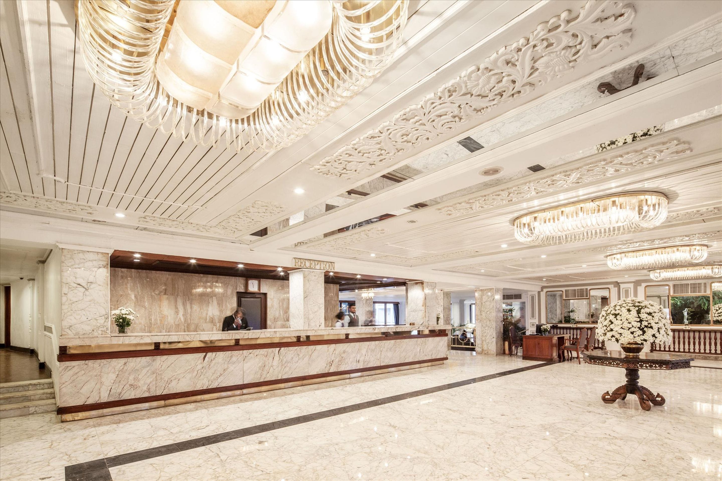 A hotel reception area with marble counters, a reception desk, and a chandelier.