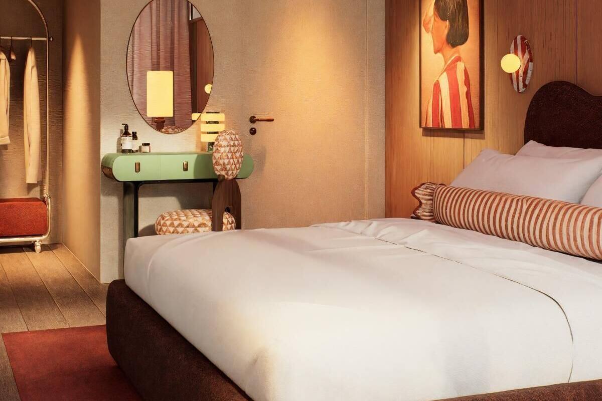 A hotel room with a bed, a round mirror, a vanity with a green cabinet, a painting on the wall, and a ceiling light fixture.