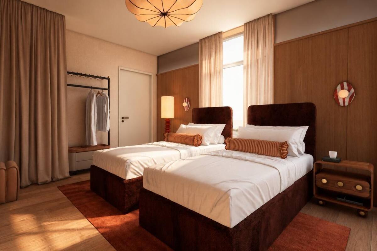 A hotel room with two beds, a wooden headboard, a bedside table with a lamp, a wardrobe, and a large window.