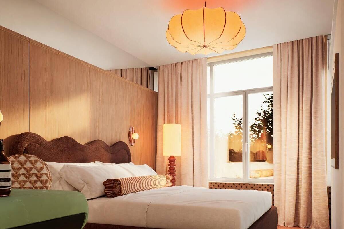 A modern hotel room with a large bed, a wooden headboard, a nightstand, a lamp, and a view of the outdoors.