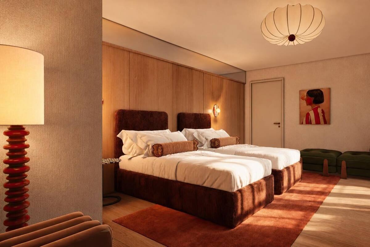 A hotel room with a double bed, a nightstand, a lamp, a green sofa, and a painting on the wall.