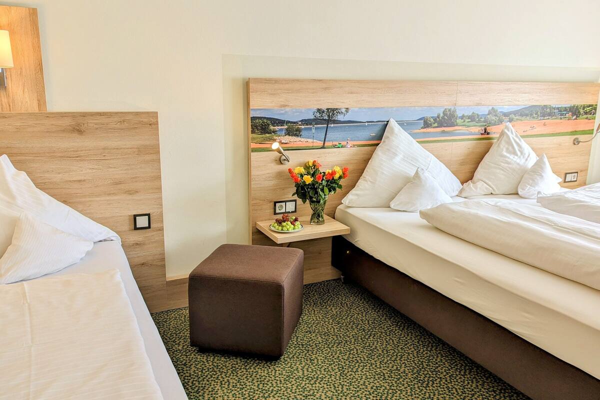 Une chambre d’hôtel avec un lit, une petite table sur laquelle est posé un vase de fleurs, et un tableau représentant un paysage accroché au-dessus de la tête de lit.