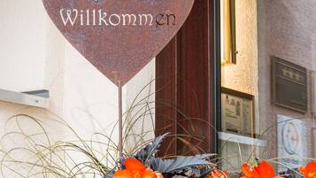 A heart-shaped sign with "Herzlich Willkommen" and a flower bed in front.