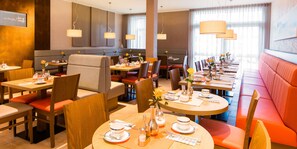 Ein modernes Restaurant mit runden Tischen, gepolsterten Sitzgelegenheiten und Pendelleuchten.