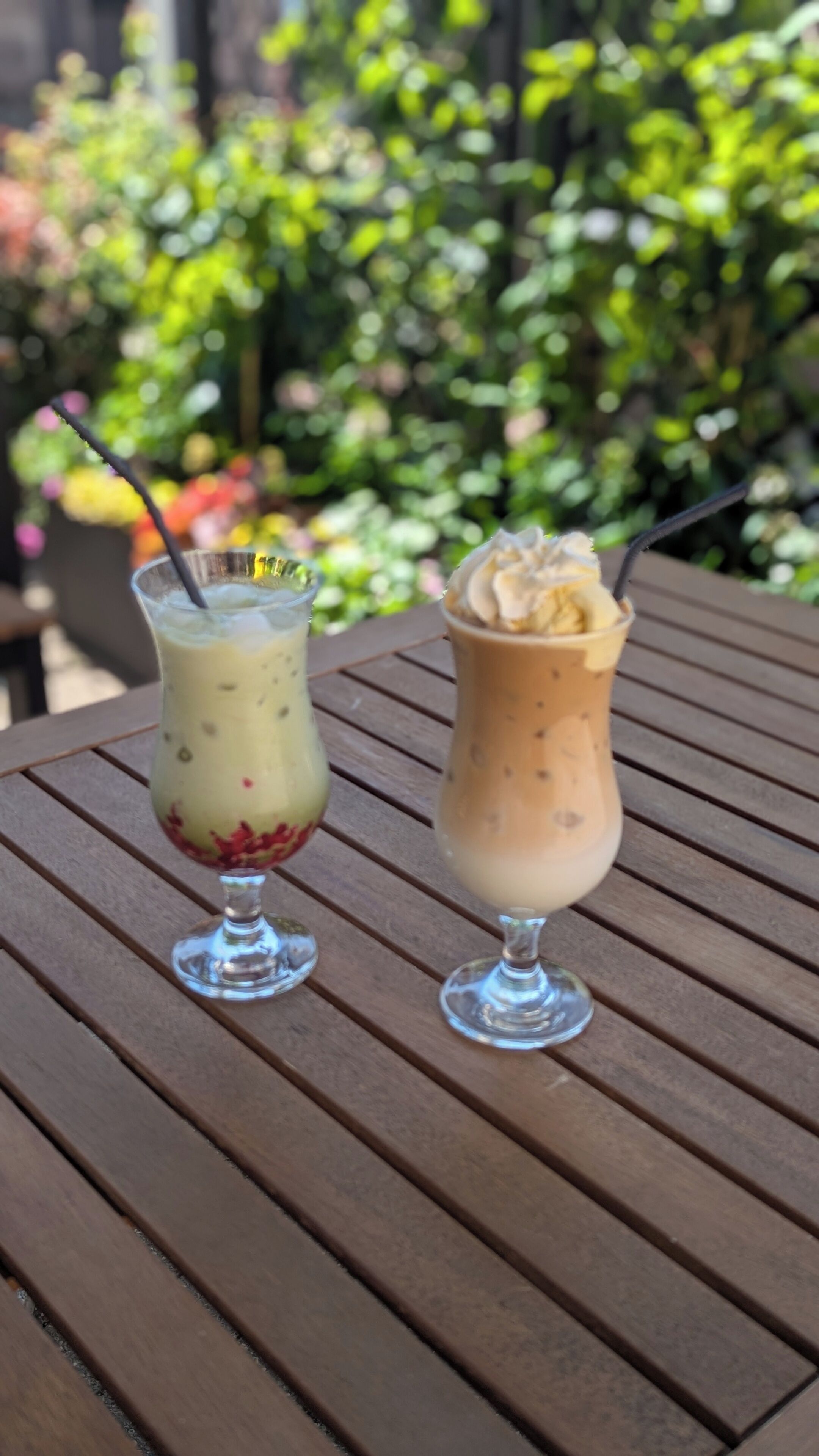 Two drinks on a wooden table with a blurred green background.