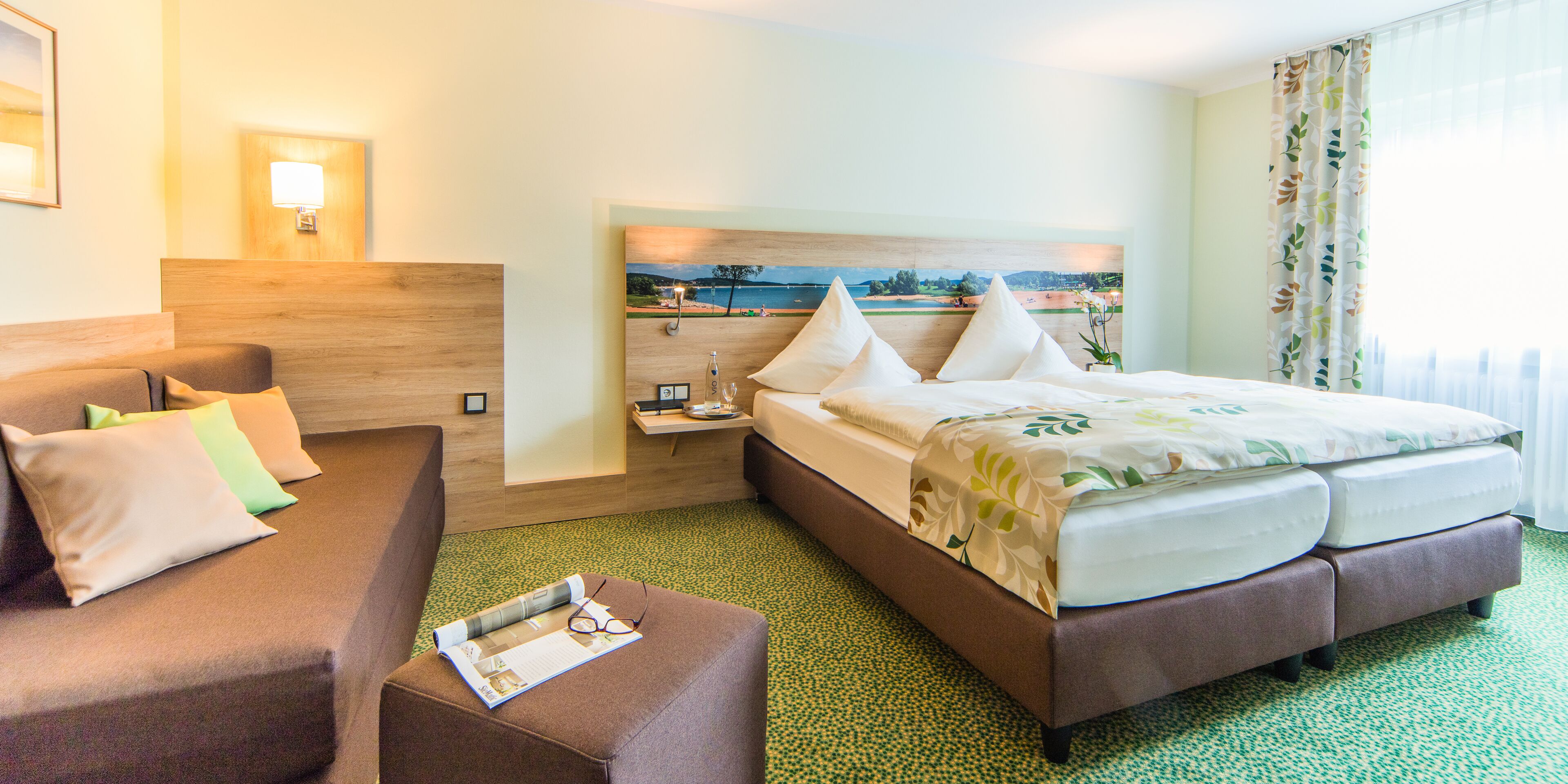 A hotel room with a bed, a sofa, a nightstand, and a painting of a beach scene.