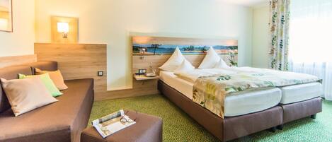 A hotel room with a bed, a sofa, a nightstand, and a painting of a beach scene.