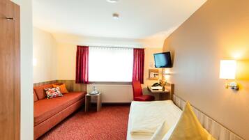 Habitación de hotel con cama, sofá, escritorio con computadora, televisor y ventana con cortinas.