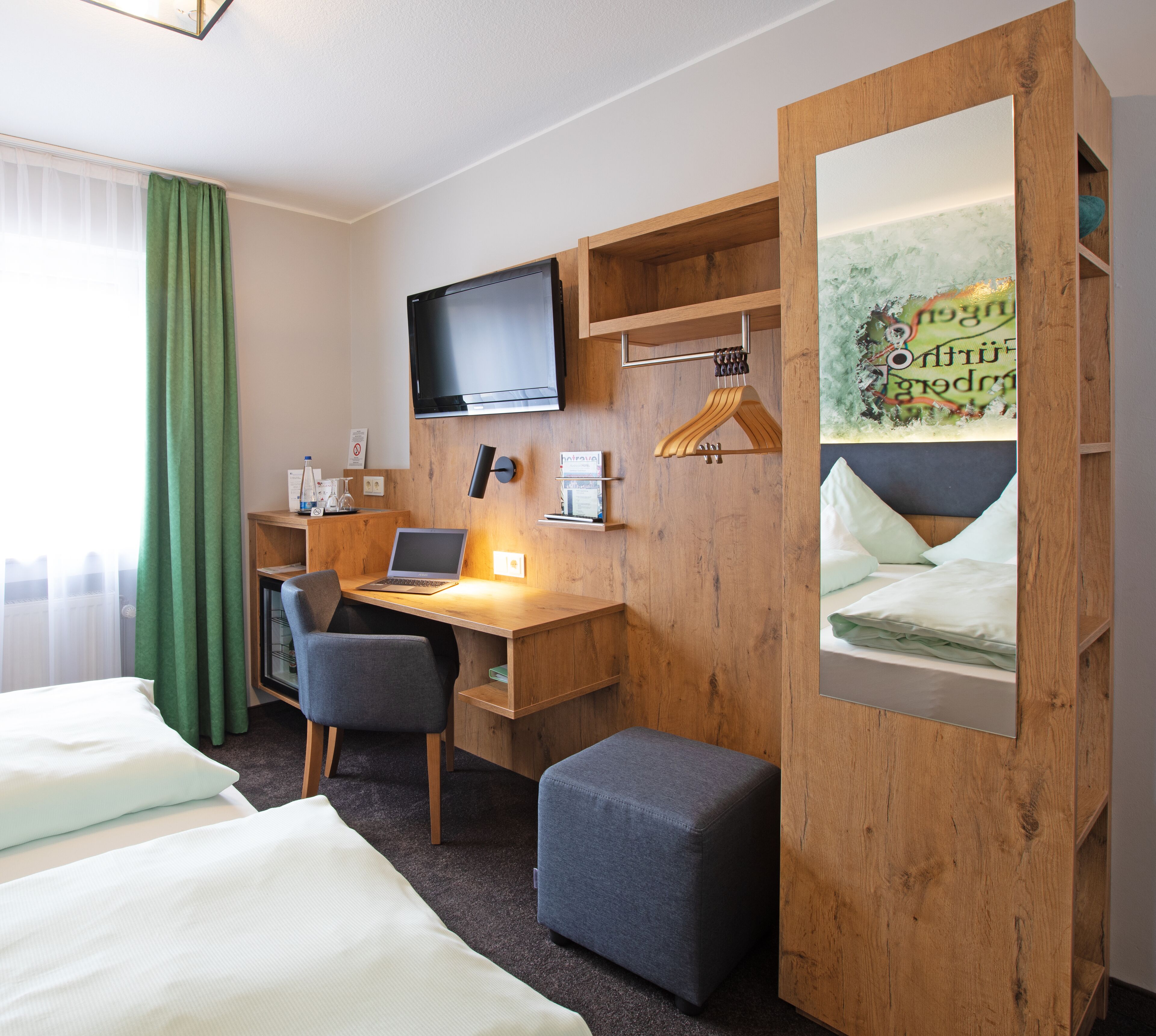 A hotel room with a wooden desk, a laptop, a television, and a bed.