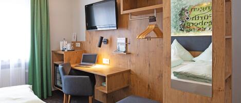 A hotel room with a wooden desk, a laptop, a television, and a bed.