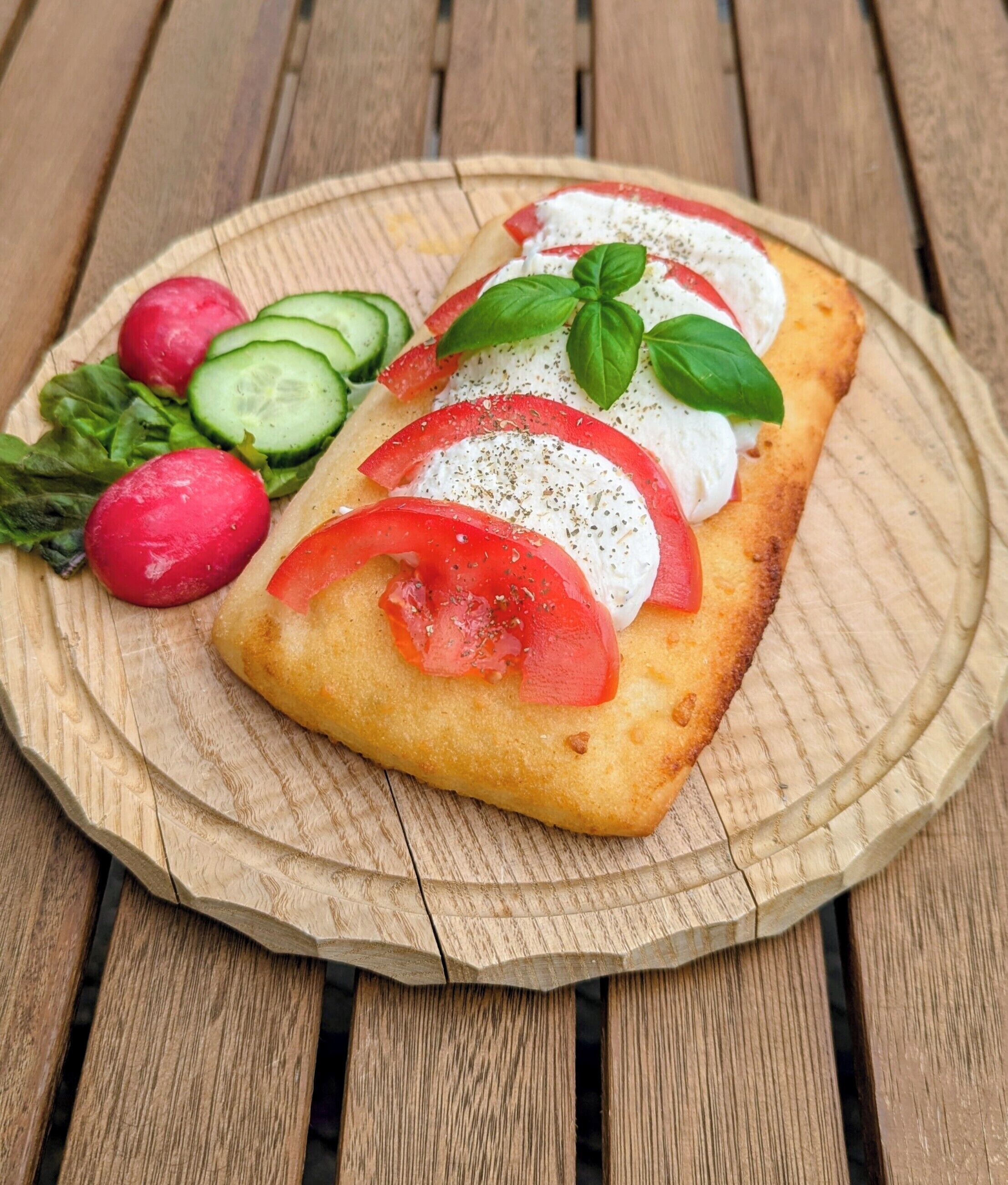 Una especie de pan plano cubierto de tomates, queso y hierbas, servido sobre una tabla de madera.