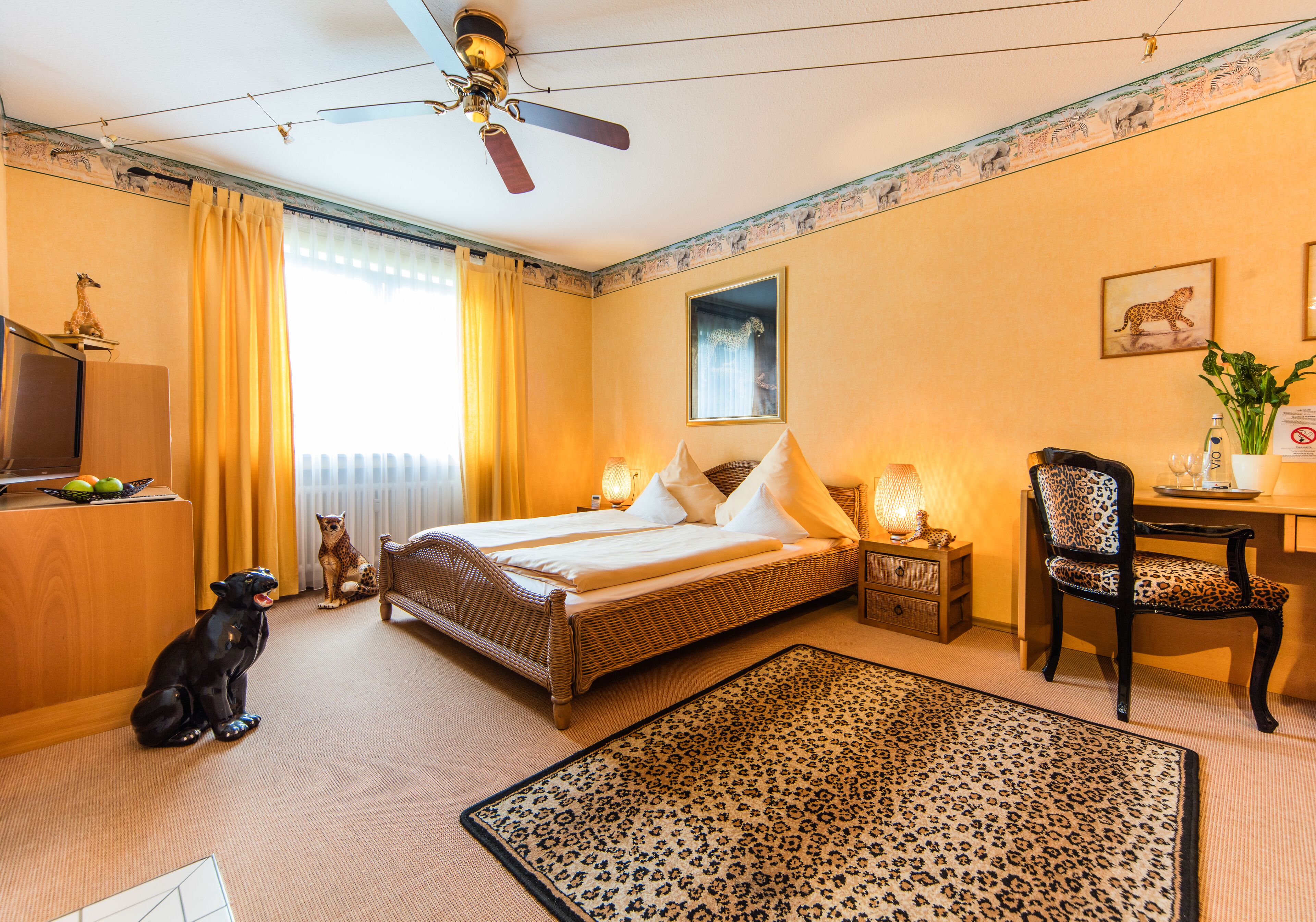 Une chambre d’hôtel avec un lit, un bureau, une chaise, un tapis et un ventilateur de plafond.