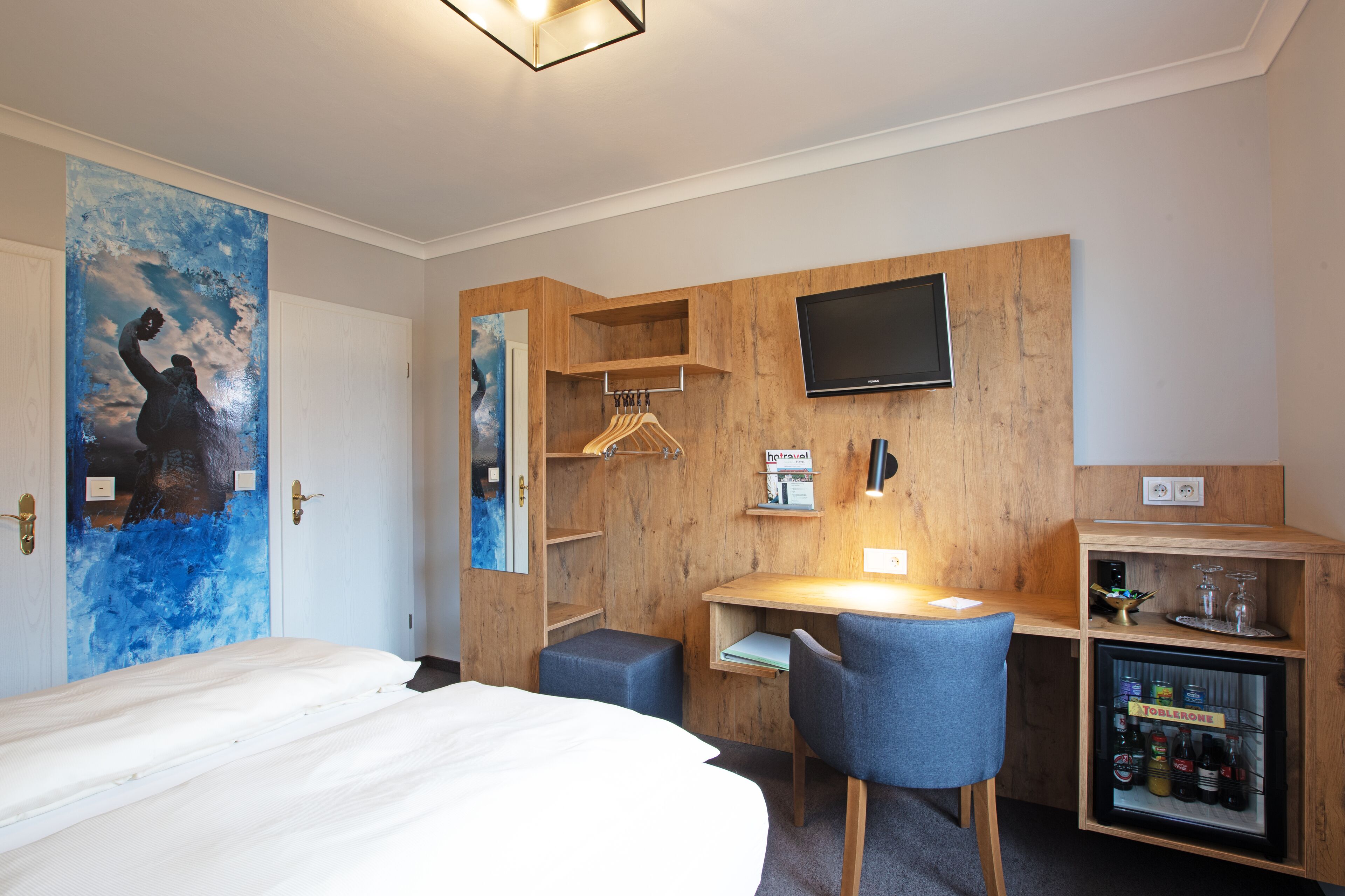 Ein Hotelzimmer mit Bett, Schreibtisch mit Stuhl, Fernseher, Kleiderschrank und einer Minibar.