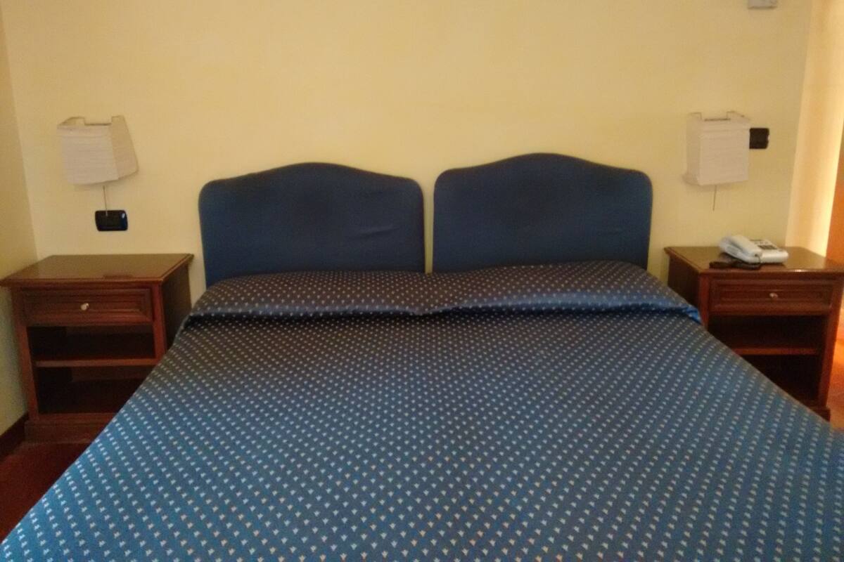 Une chambre d’hôtel standard, équipée d’un lit double, de deux tables de chevet, d’une lampe et d’un téléphone.