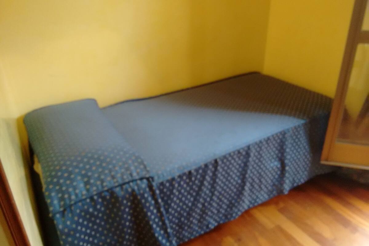 Une petite pièce fermée, avec un couvre-lit à motifs bleus et un plancher en bois.