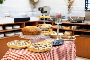 Una mesa de buffet con diversas opciones de repostería, incluyendo tartas y pasteles, sobre un mantel a cuadros.