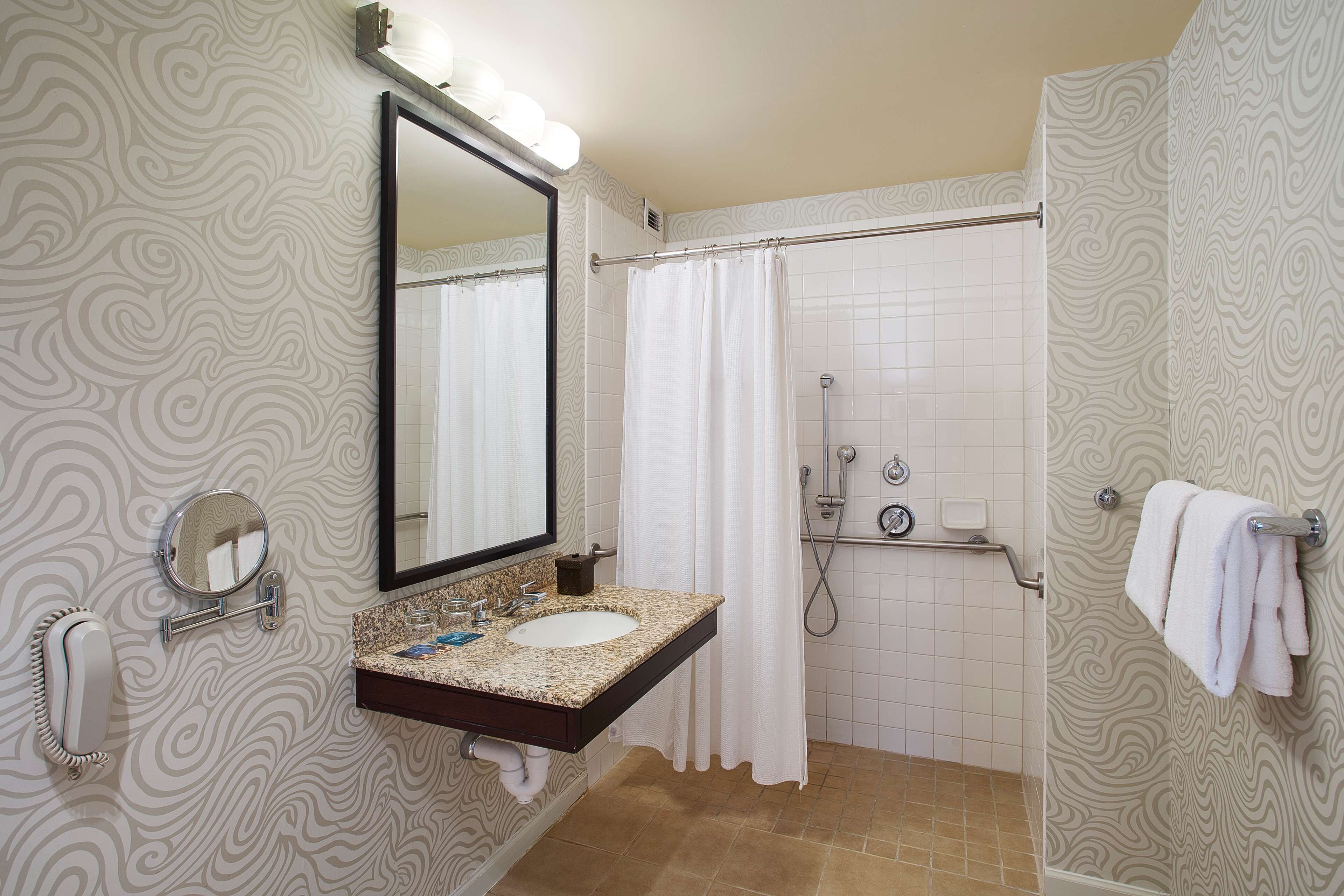 Un baño con tocador, un espejo grande, ducha y toallero.