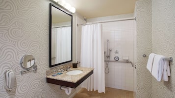 Un baño con tocador, un espejo grande, ducha y toallero.