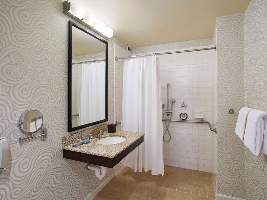 Une salle de bain avec un meuble-lavabo, un grand miroir, une douche et un porte-serviettes.