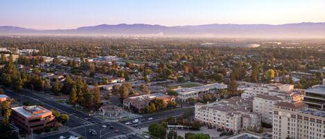 An aerial view of a cityscape with a mix of residential and commercial buildings, roads, and a distant mountain range.