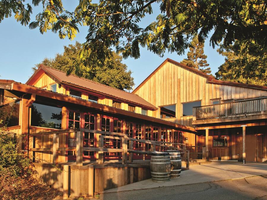 A wooden building with large windows and a balcony, surrounded by trees.