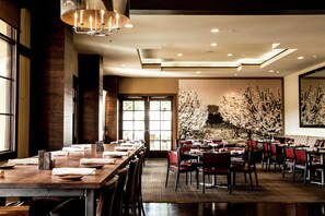 A spacious dining area with long tables and red chairs, large windows, and a wall with a floral mural. - Juniper Hotel Cupertino, Curio Collection by Hilton (Cupertino)
