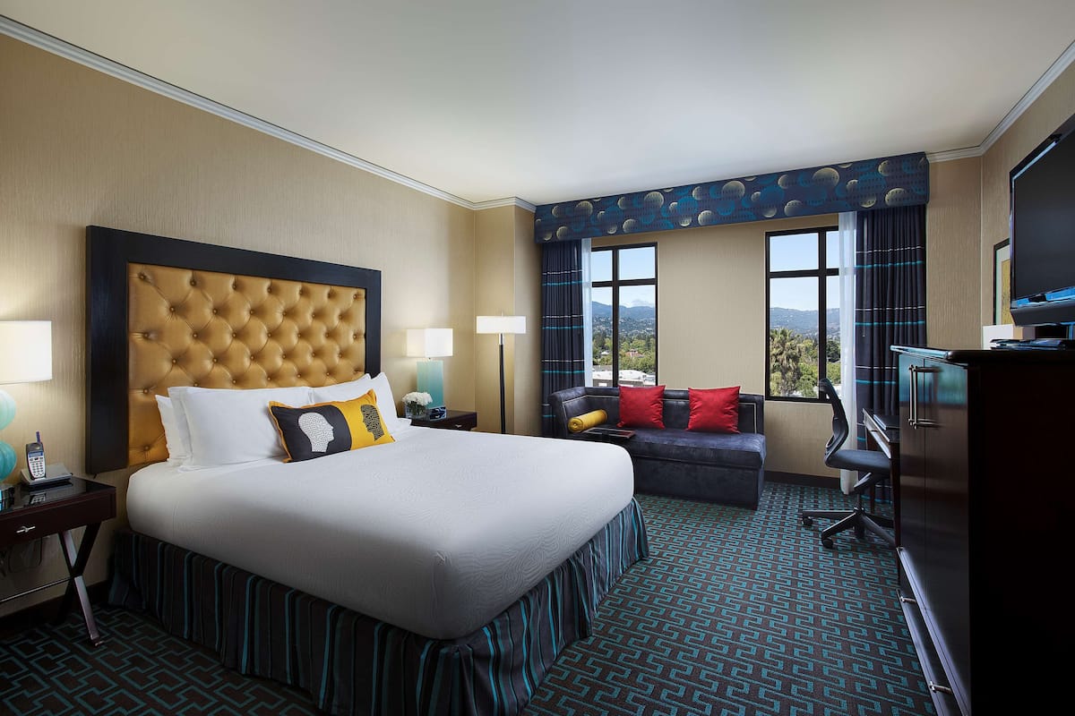 A hotel room with a large bed, a sofa, a desk, and a TV.