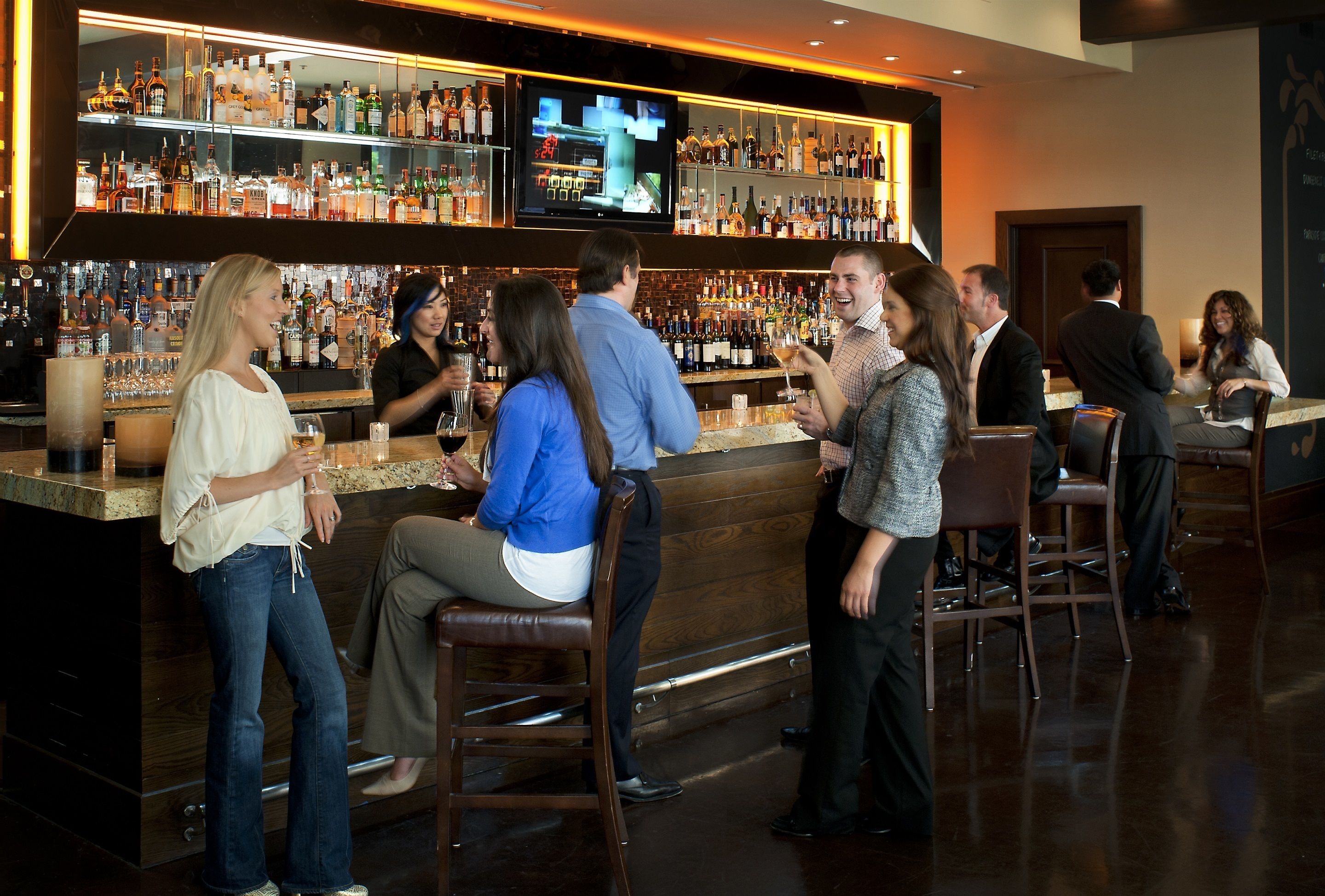 A bar area with a variety of liquor bottles, a television screen, and several patrons.