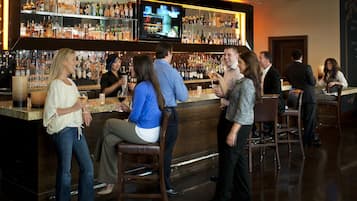 A bar area with a variety of liquor bottles, a television screen, and several patrons.