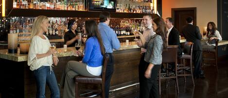 A bar area with a variety of liquor bottles, a television screen, and several patrons.
