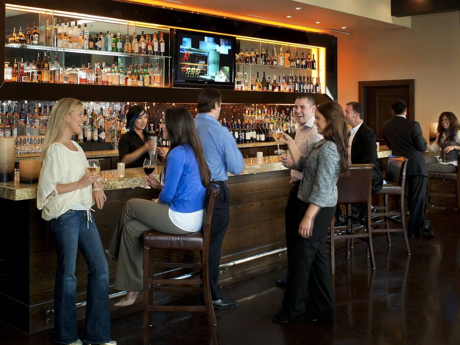 A bar area with a variety of liquor bottles, a television screen, and several patrons.
