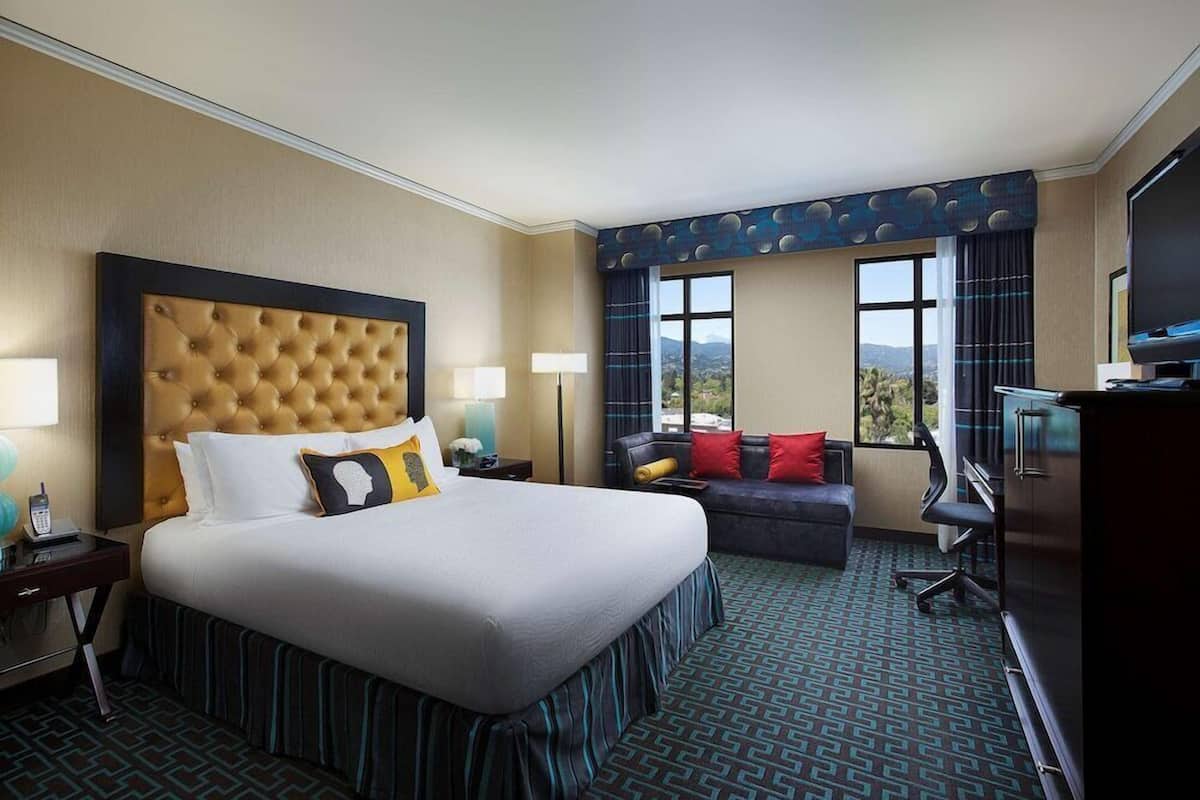 A hotel room with a large bed, a sofa, a desk, and a TV.