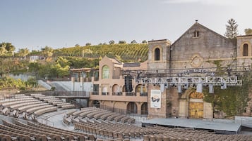 Un amphithéâtre en plein air doté de gradins et d’une scène, entouré de bâtiments historiques et de vignobles.