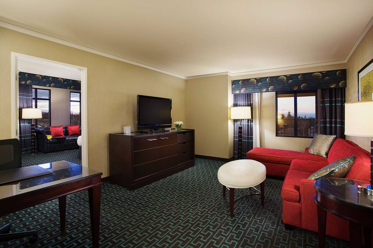 A hotel room with a large bed, a TV on a dresser, a desk with a chair, and a red sofa.