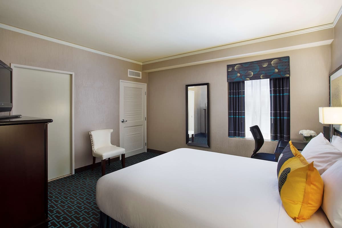 A hotel room with a bed, a desk, a chair, a mirror, and a window with curtains.