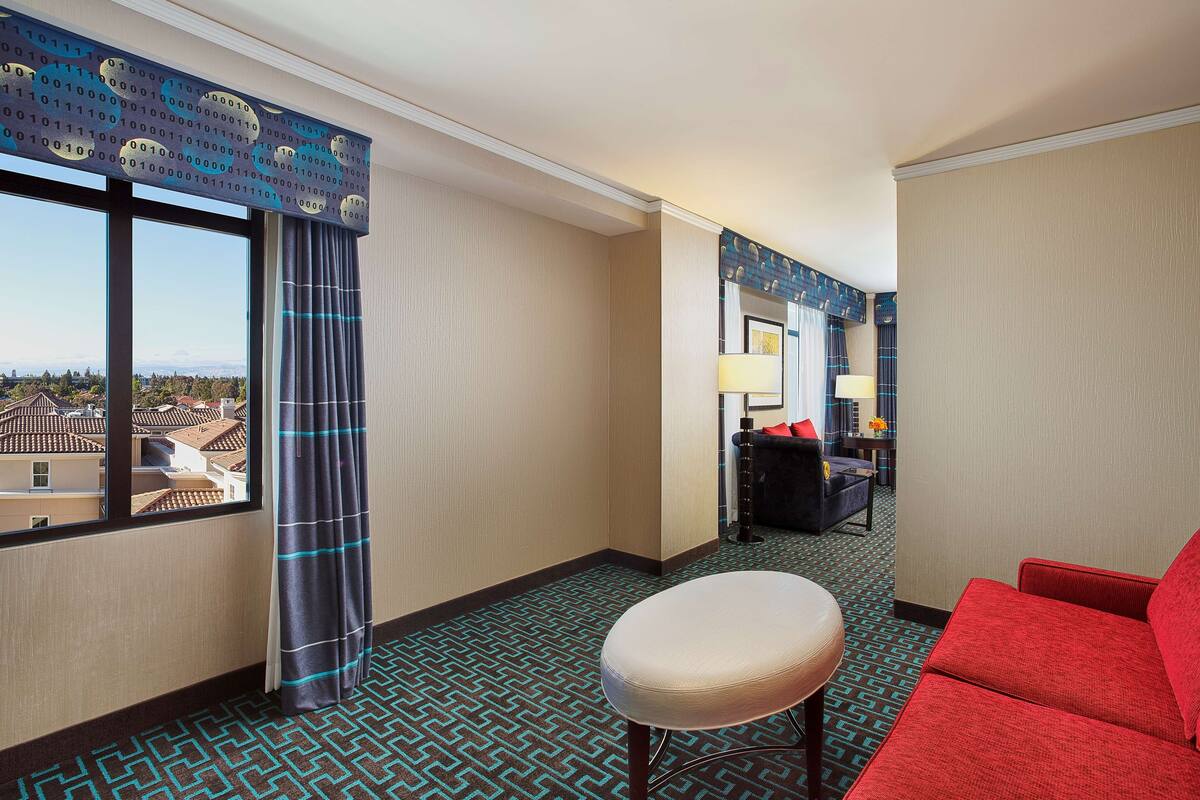 A hotel room with a large window, a red sofa, a small round table, and a patterned carpet.