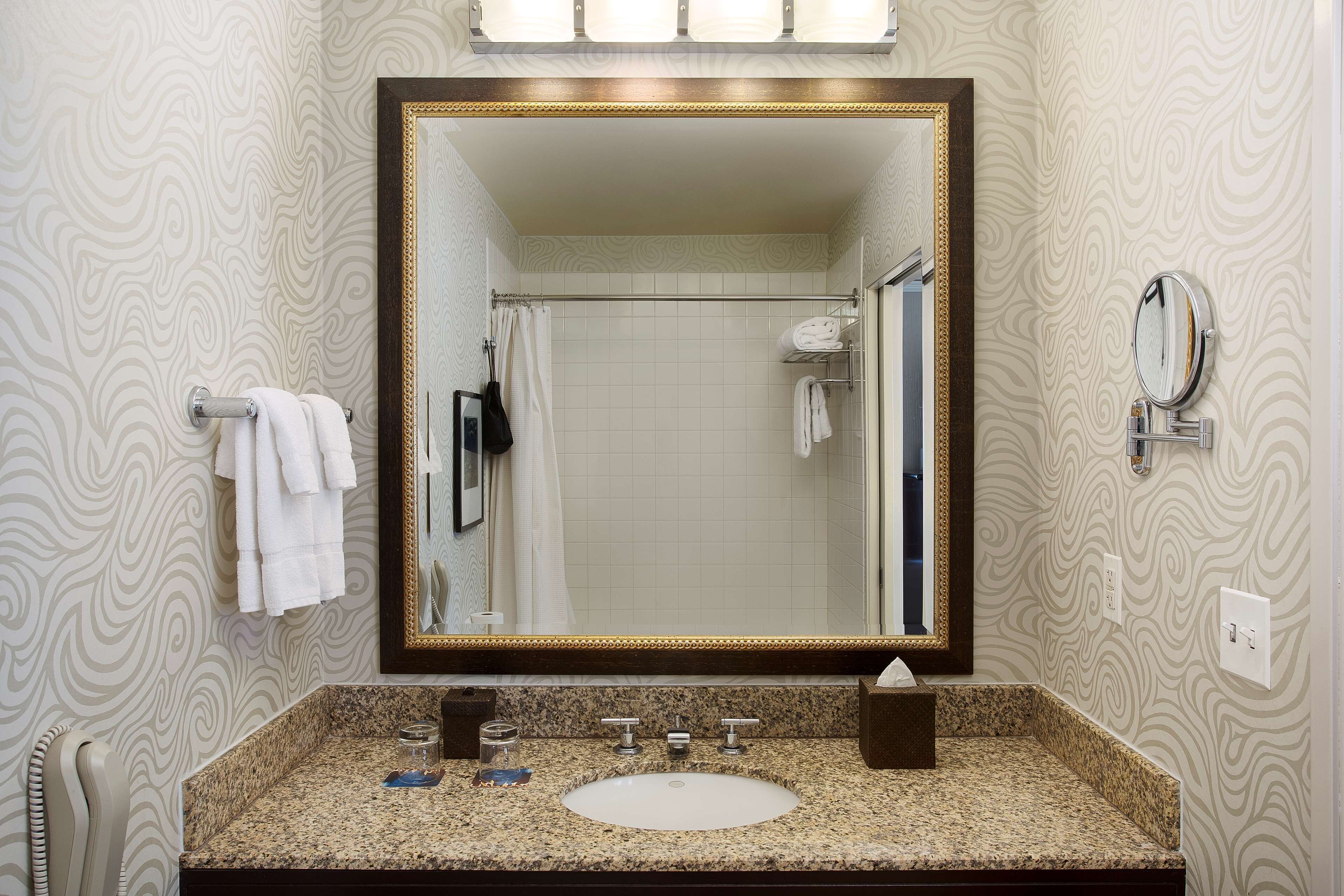 Un bagno con un ampio specchio, un lavabo con due rubinetti e un portaservizi con diversi asciugamani bianchi.