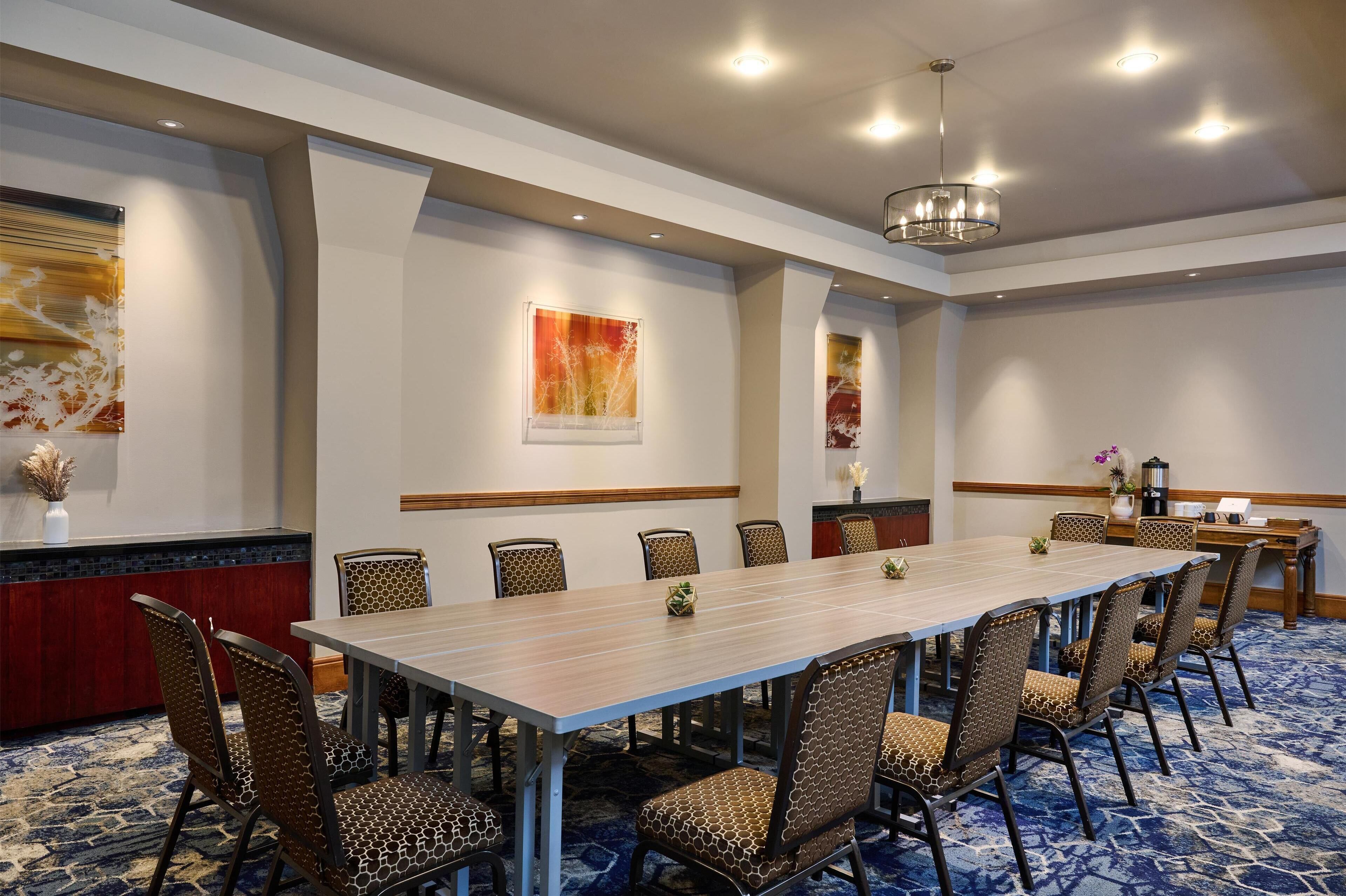 A conference room with a long table, patterned chairs, a red accent wall, and abstract art.