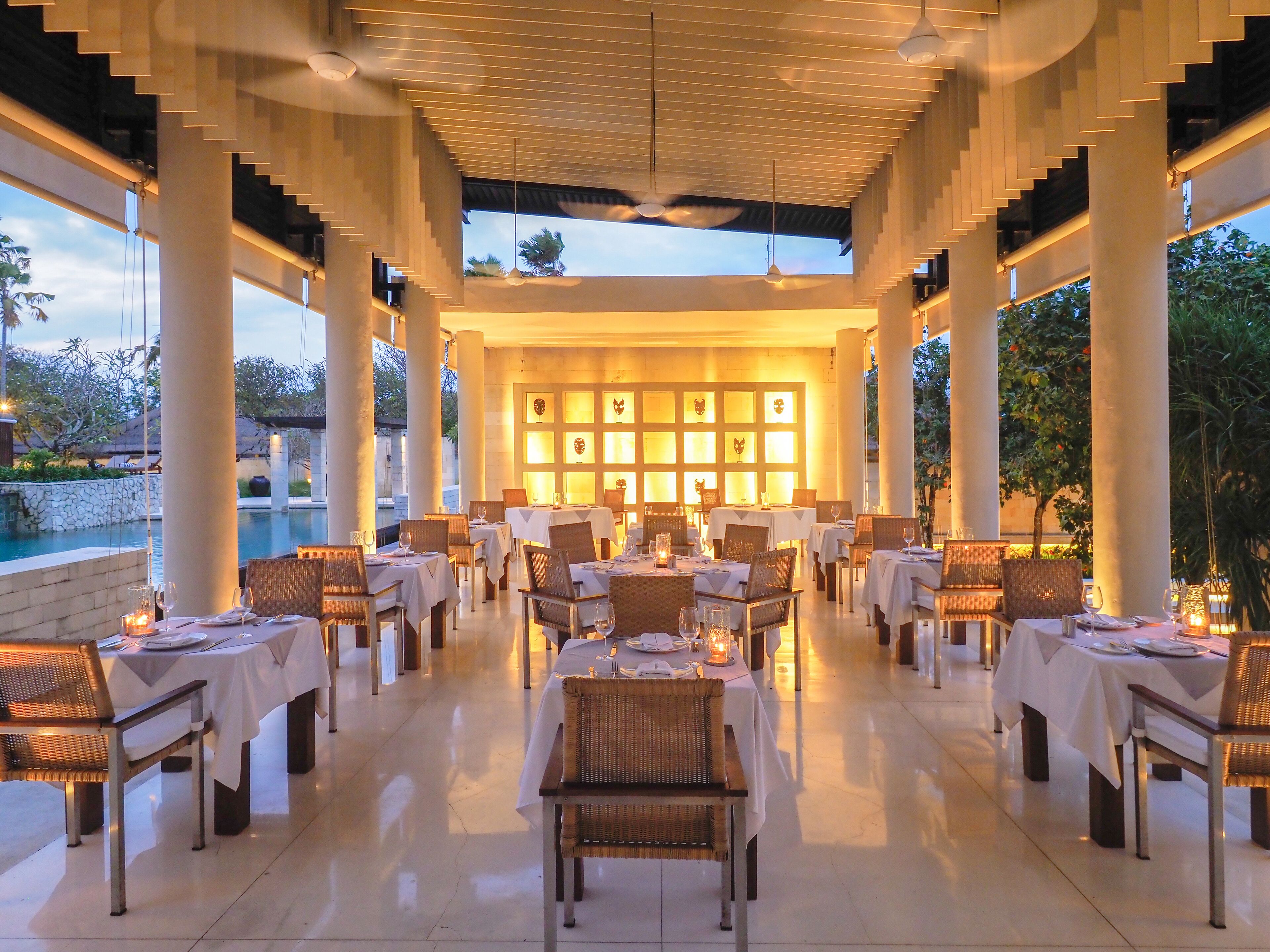 A restaurant with tables set for dining, a pool in the background, and a view of the sky.