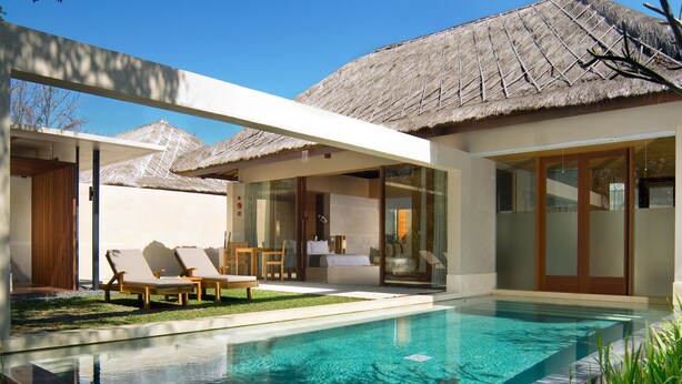 Um resort moderno com piscina, cadeiras de sol e uma estrutura com telhado de palha.