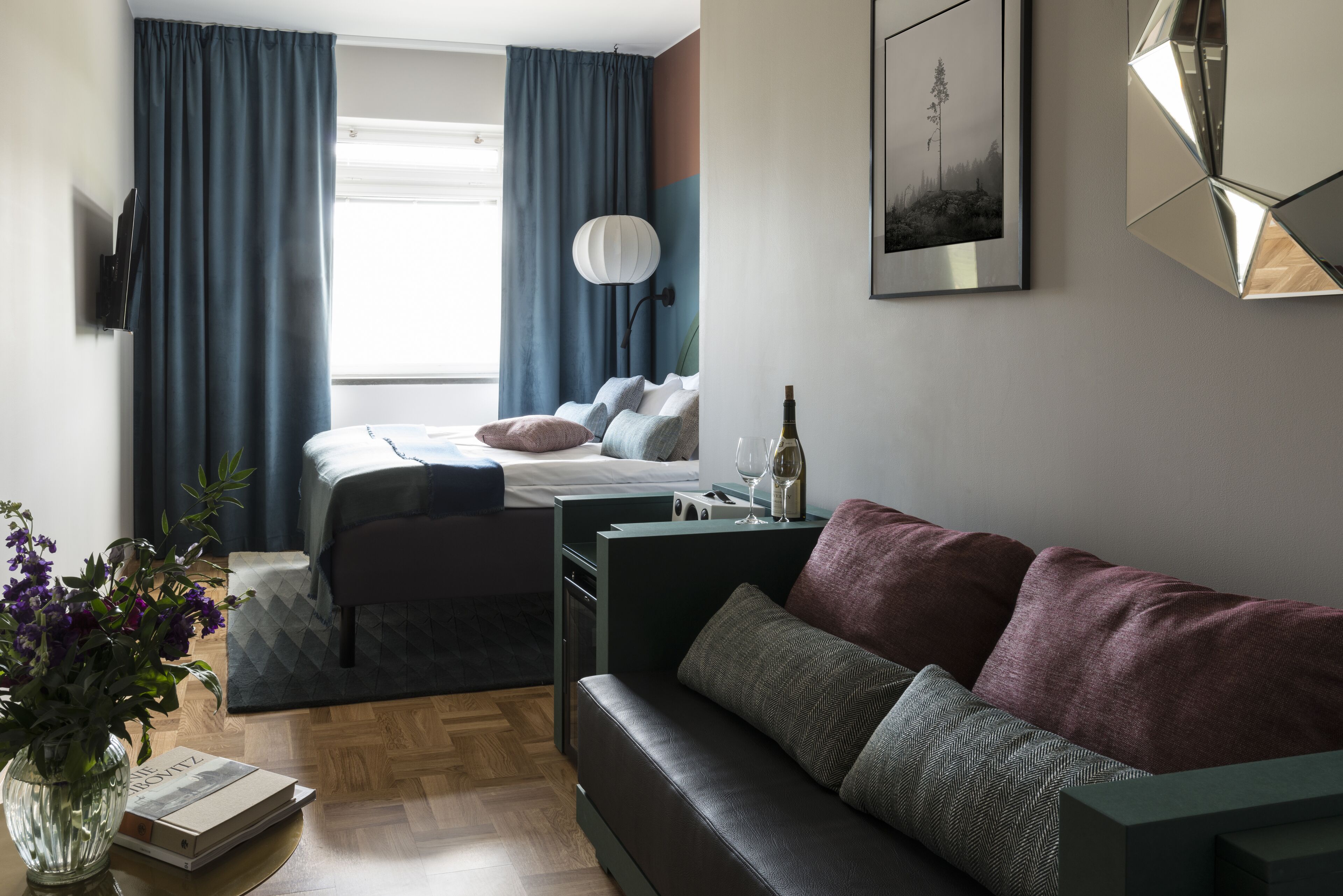 Quarto moderno com cama, mesa de cabeceira, luminária e vista para o exterior.