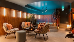 A modern lounge area with a curved ceiling, wooden panel walls, and a seating arrangement including two armchairs and a round ottoman. - Näsby Slott (Taby)
