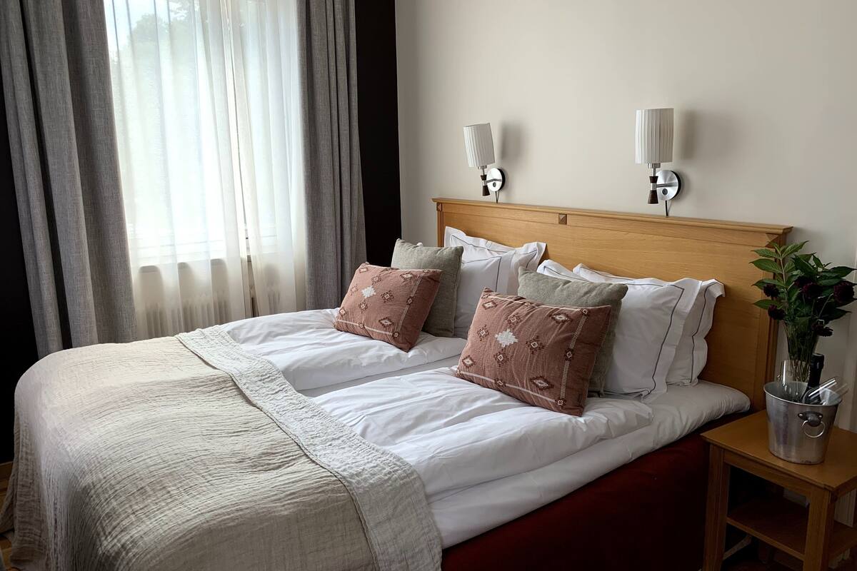 A neatly made bed with white and brown bedding, a wooden headboard, and two wall-mounted lamps.