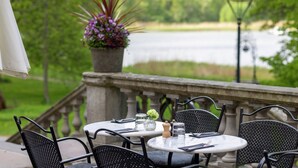 An outdoor patio with round tables and chairs, a potted plant, and a view of a lake. - Näsby Slott (Taby)