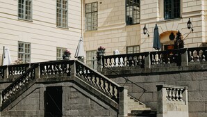 A stone staircase with balustrades leading to a building with multiple windows and a balcony with potted plants. - Näsby Slott (Taby)