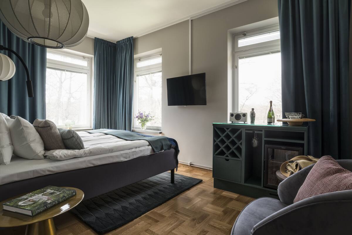 A modern bedroom with a bed, a TV, a small table, and a seating area.