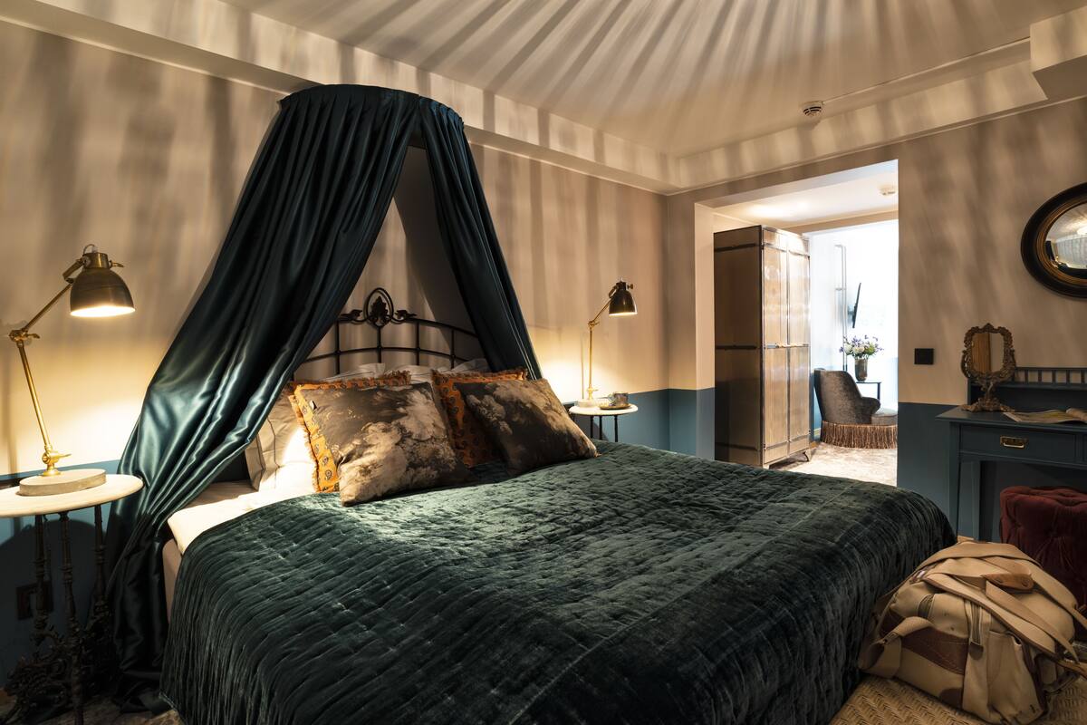 A bedroom with a canopy bed, bedside lamps, a dresser, and a mirror.