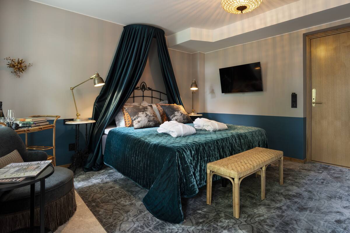 A bedroom with a bed, a bedside table, a chair, a bench, a TV, and a door.