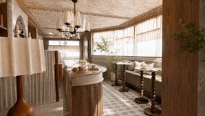 A room with a wooden bar, a seating area with a sofa and round tables, and a decorative ceiling with a chandelier. - Villa Nord (Trondheim)